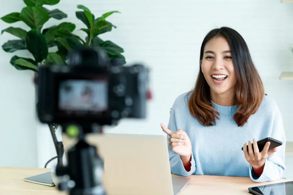 vlogger in blue sweater presenting to a DSLR camera on a tripod