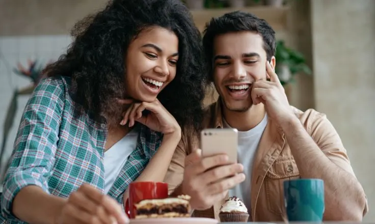 two people smiling at phone while eating baked goods
