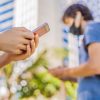 person using phone with another wearing mask in the background