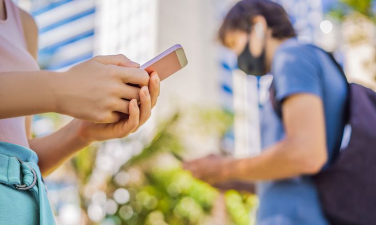 person using phone with another wearing mask in the background