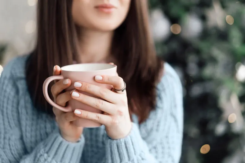 woman holding mug in front of a decorated tree