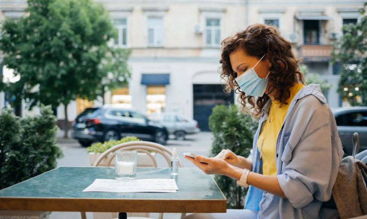 woman wearing a mask, sitting outside using her phone