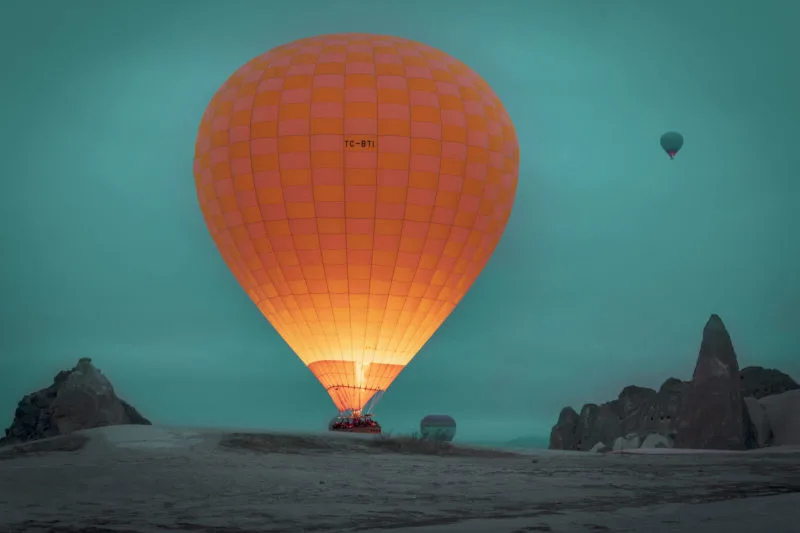 orange hot air balloon lit up at dusk in the mountains