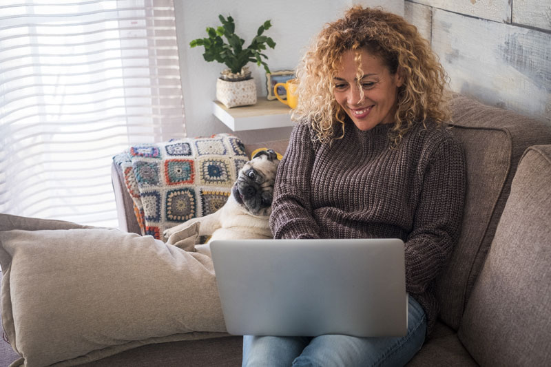woman sitting on couch with dog, looking at her laptop