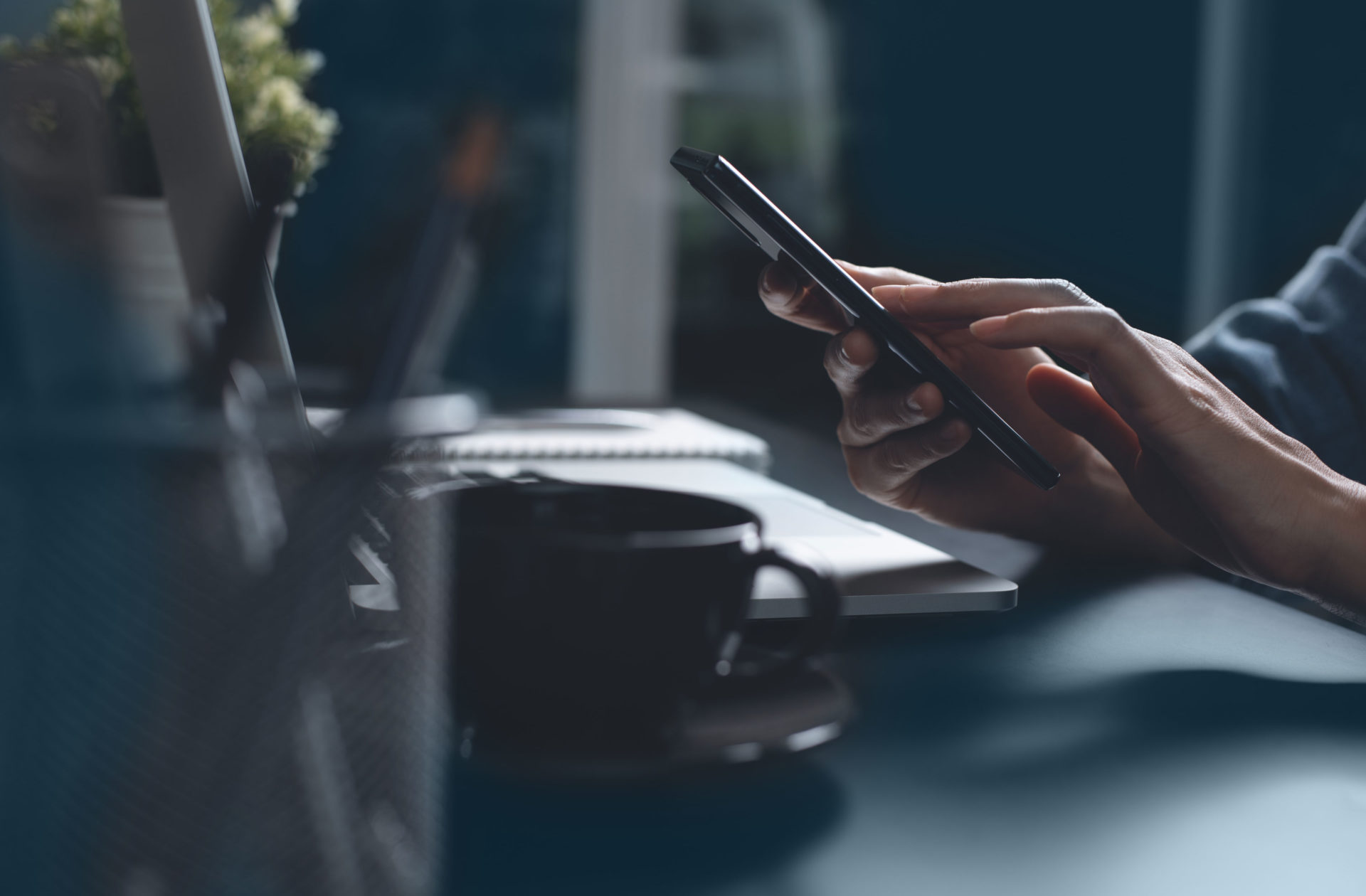 hands using a smartphone at a desk with a computer in a dark room