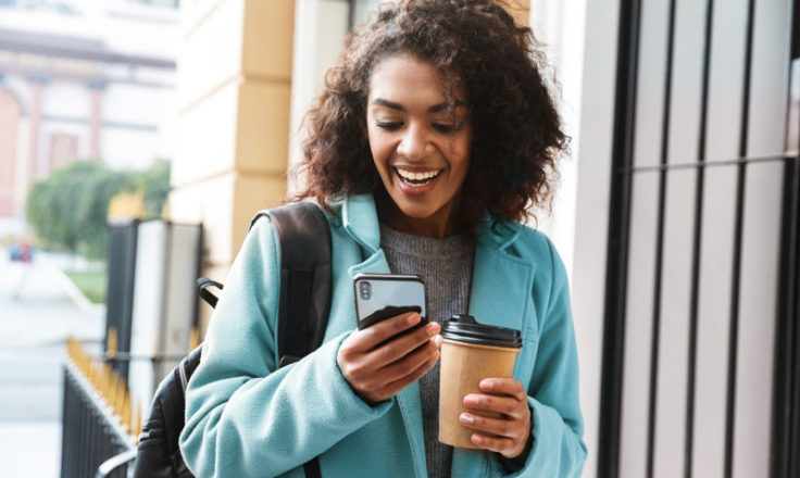 woman smiling at phone holding coffee