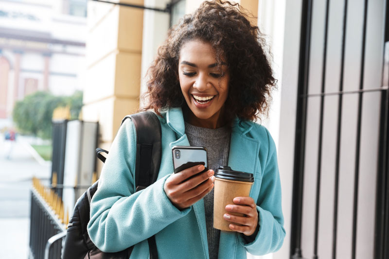 woman smiling at phone holding coffee