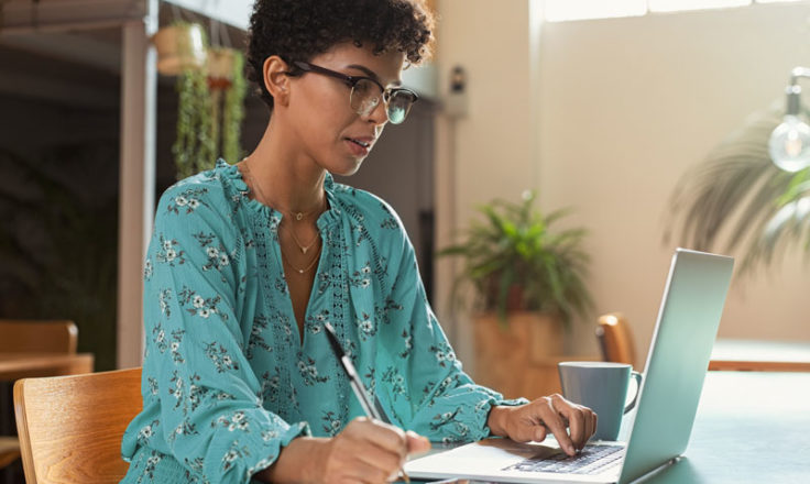 woman using laptop and taking notes