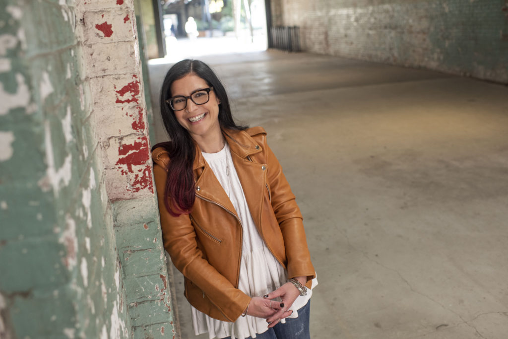 Jamie Lieberman laughing and leaning up against a brick wall