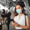 woman wearing mask using phone at train station