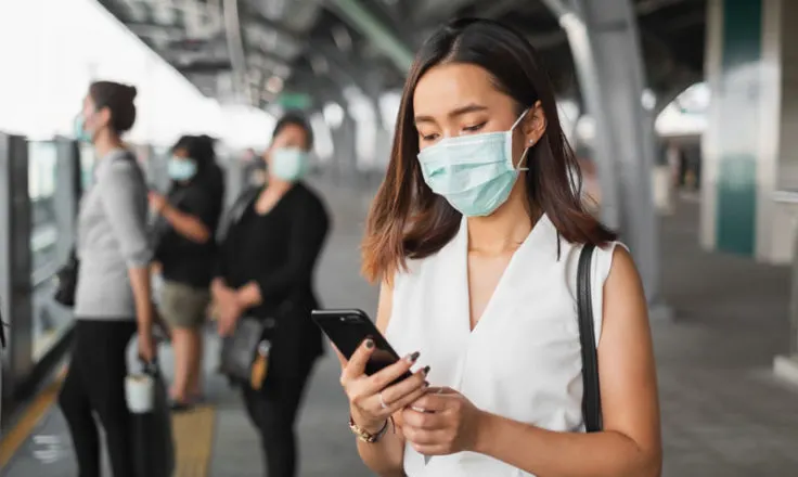 woman wearing mask using phone at train station