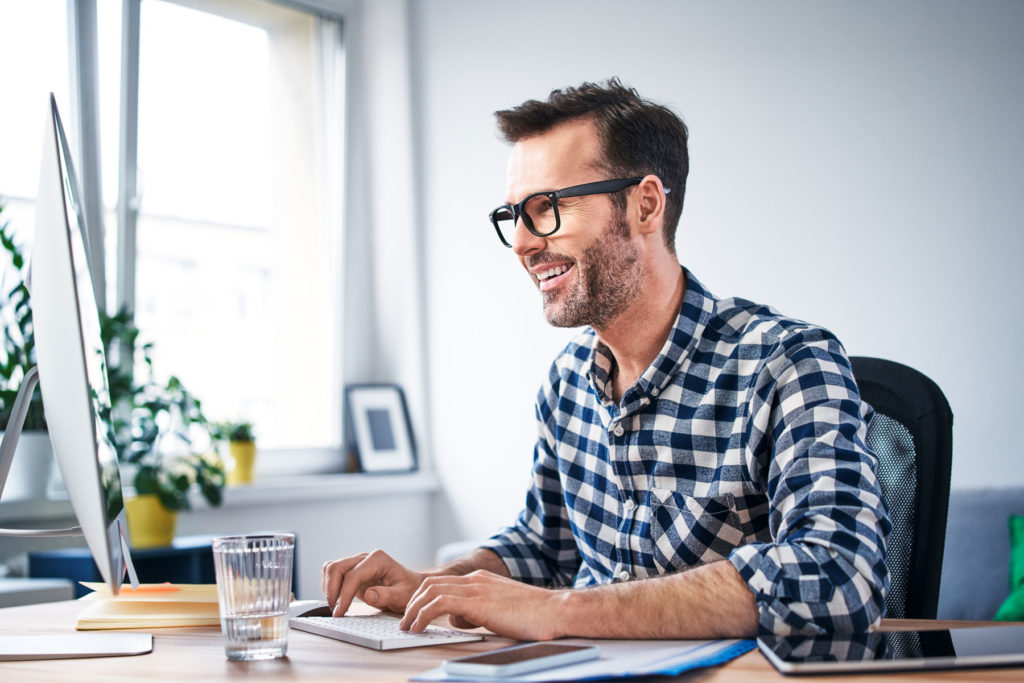 man in a blue and white plaid shirt using a desktop computer at a desk