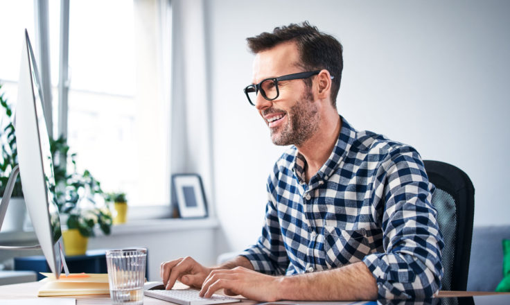 man in a blue and white plaid shirt using a desktop computer at a desk