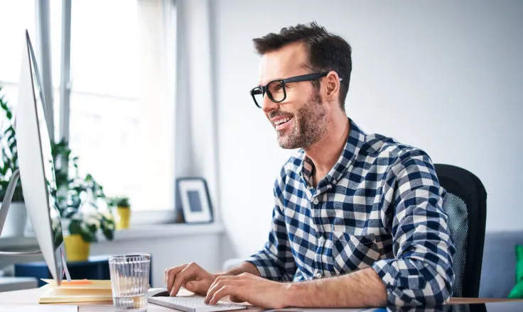 man in a blue and white plaid shirt using a desktop computer at a desk