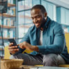 man sitting on couch, looking at phone and smiling