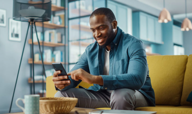 man sitting on couch, looking at phone and smiling