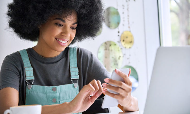 woman wearing overalls using phone at a table