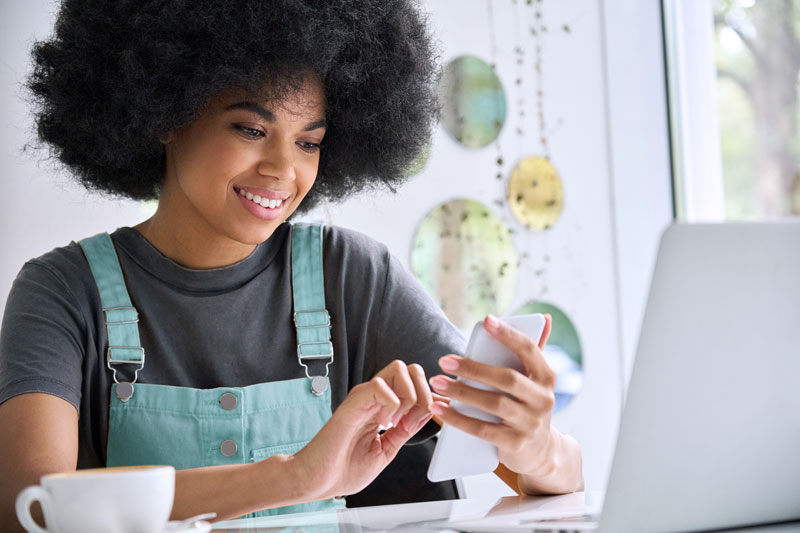 woman wearing overalls using phone at a table