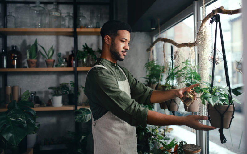 person wearing an apron facing to the right, misting plants